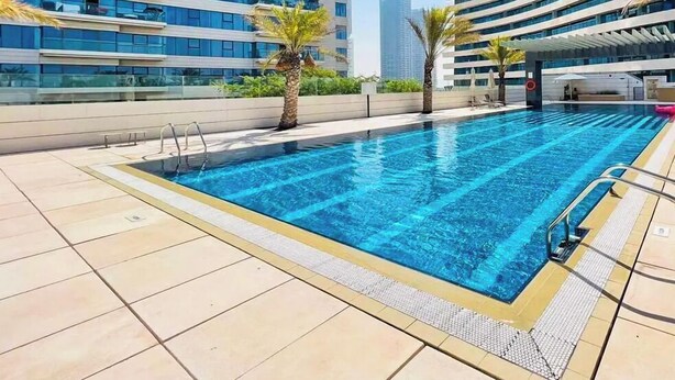 En swimmingpool med kristallklart blått vatten, omgiven av kakelplattor och palmer.