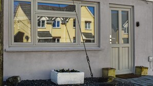 A building with a large window reflecting neighboring houses, a white door, and a small white planter with plants.