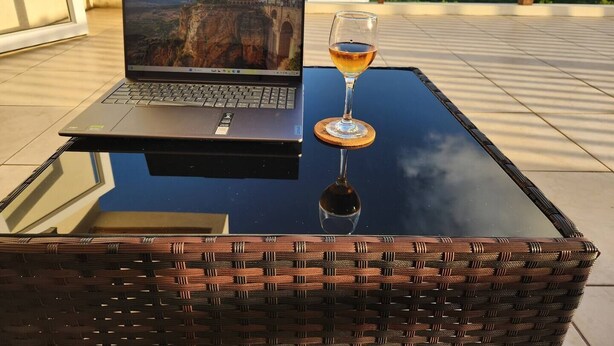 Um laptop sobre uma mesa de vidro, com uma taça de vinho ao lado.