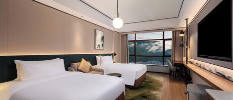 Quarto de hotel moderno com duas camas, uma escrivaninha, uma televisão grande e vista para montanhas.