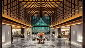 A spacious lobby with a high ceiling featuring a geometric pattern, a central seating area with tables and chairs, and a large window providing a view of greenery outside. - Hilton Garden Inn Zhangjiajie Wulingyuan (Zhangjiajie)