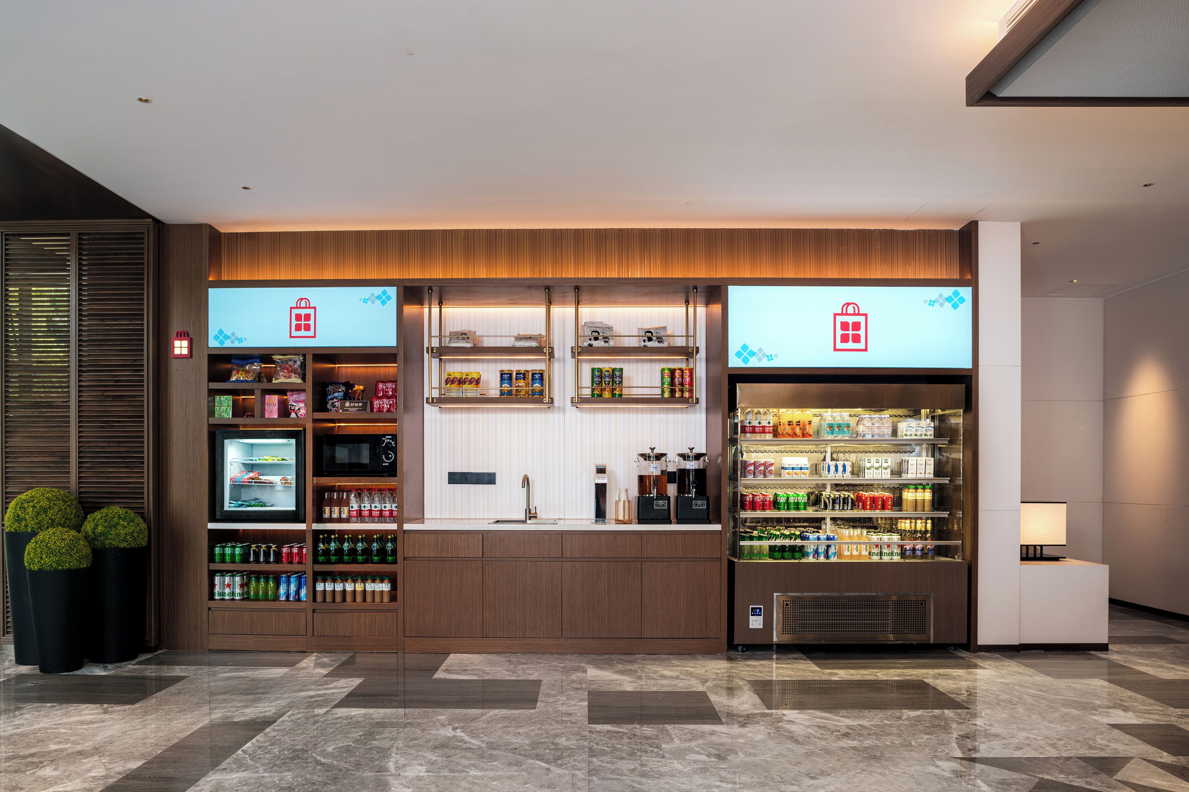 Een moderne hotel lobby met een automaat voor drankjes, een receptiebalie en een groot scherm waarop het hotel logo wordt weergegeven.