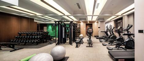 Ein modernes Fitnessstudio mit verschiedenen Trainingsgeräten, darunter Laufbänder, Crosstrainer und Kurzhanteln.