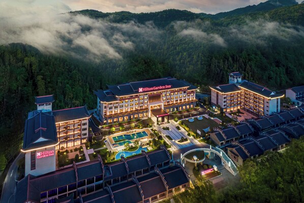 A multi-story hotel with a pool, surrounded by forested hills. - Hilton Garden Inn Zhangjiajie Wulingyuan (Zhangjiajie)