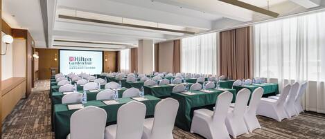 A conference room with rows of tables, chairs, and a projection screen displaying Hilton Garden Inn branding.