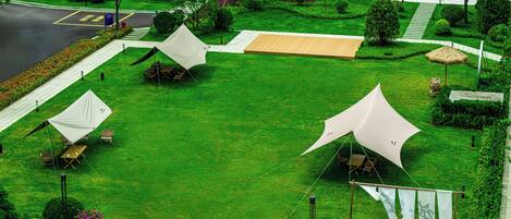 Un césped cuidado con varias tiendas de campaña y mesas, lo que sugiere un camping o un espacio para eventos al aire libre.