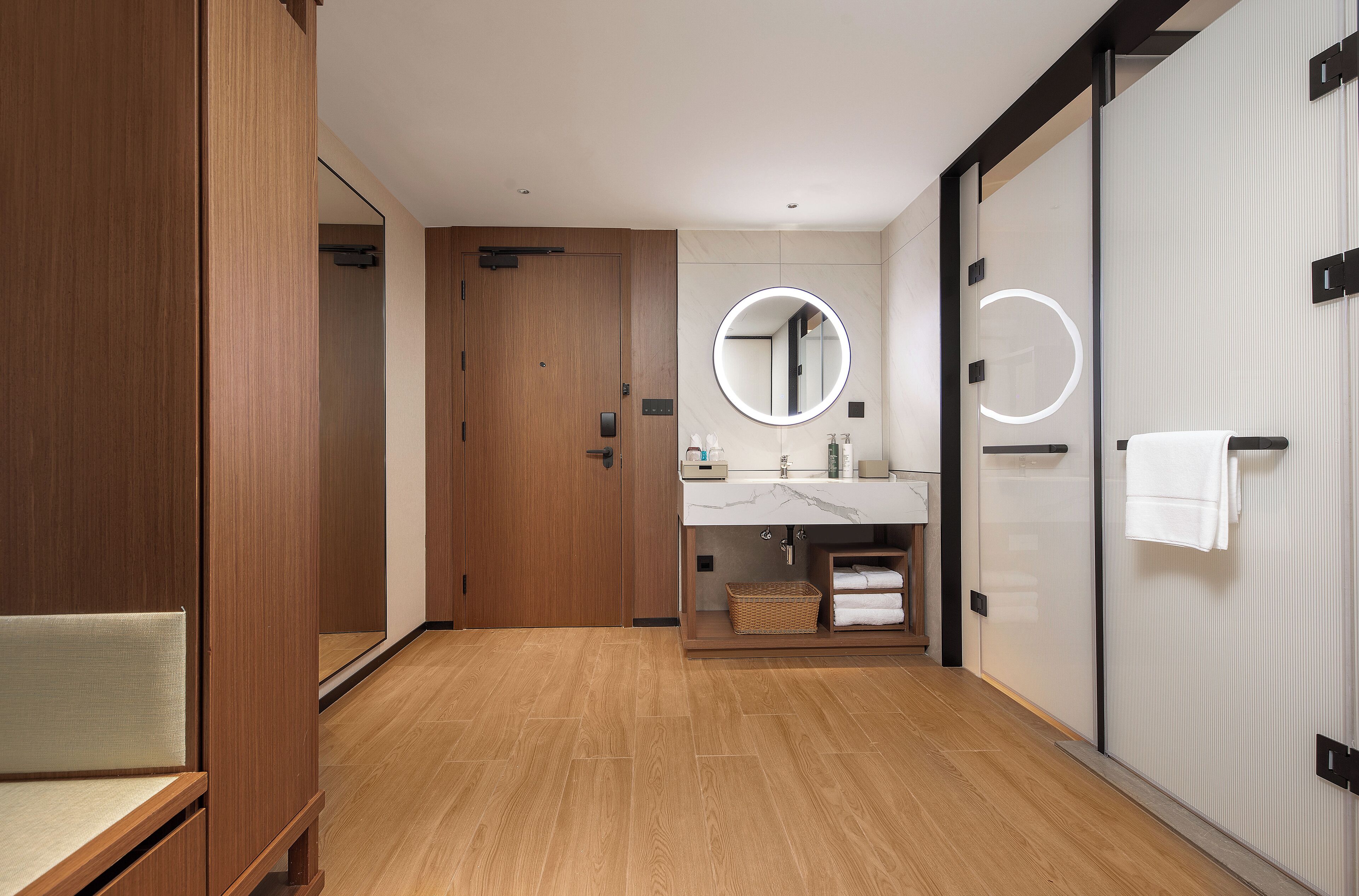 A modern bathroom with wooden flooring, a large mirror, a sink with a marble countertop, and a towel rack.