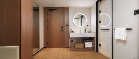 A modern bathroom with wooden flooring, a large mirror, a sink with a marble countertop, and a towel rack.