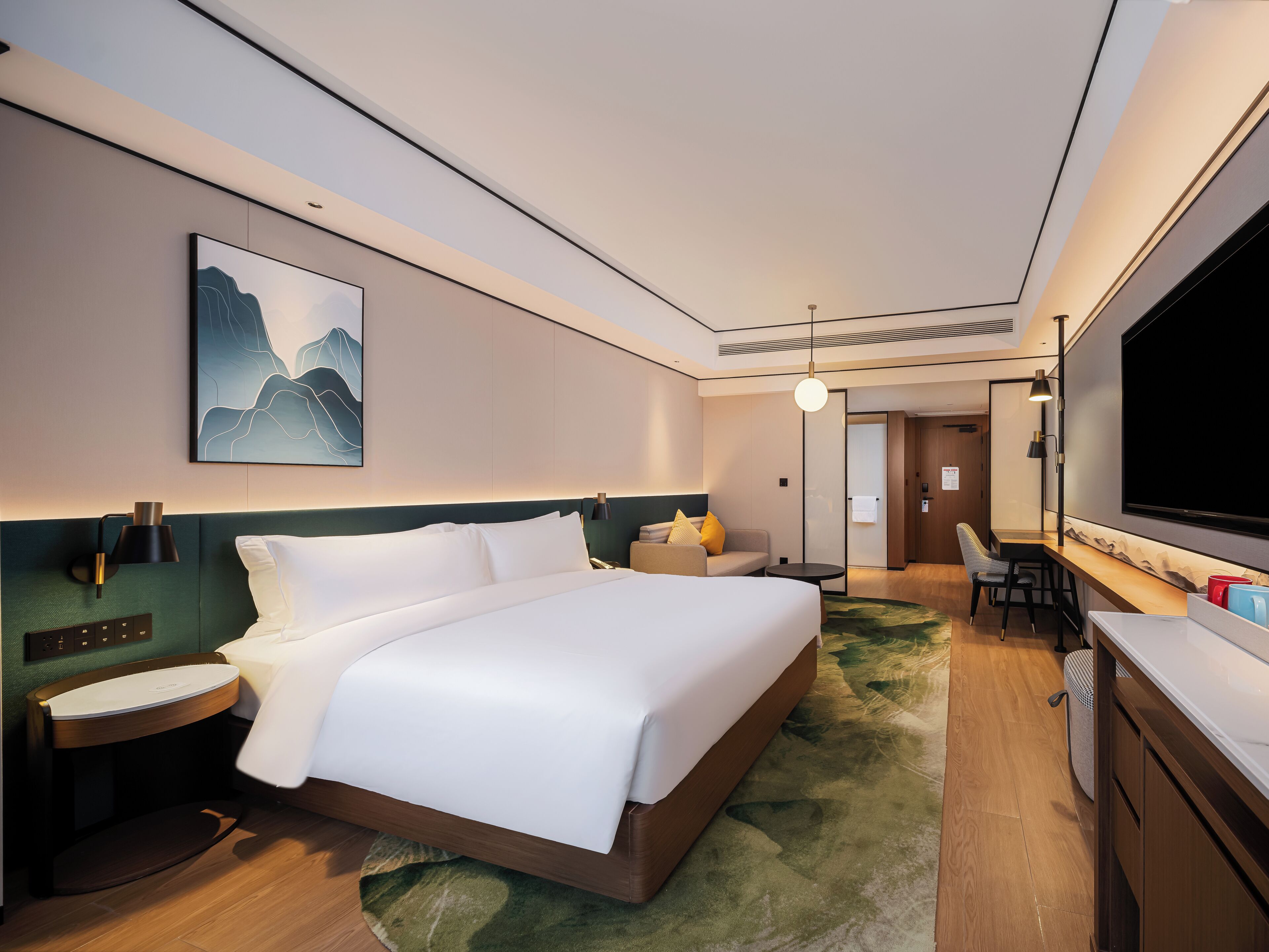 A modern hotel room with a large bed, a desk, a chair, and a television.