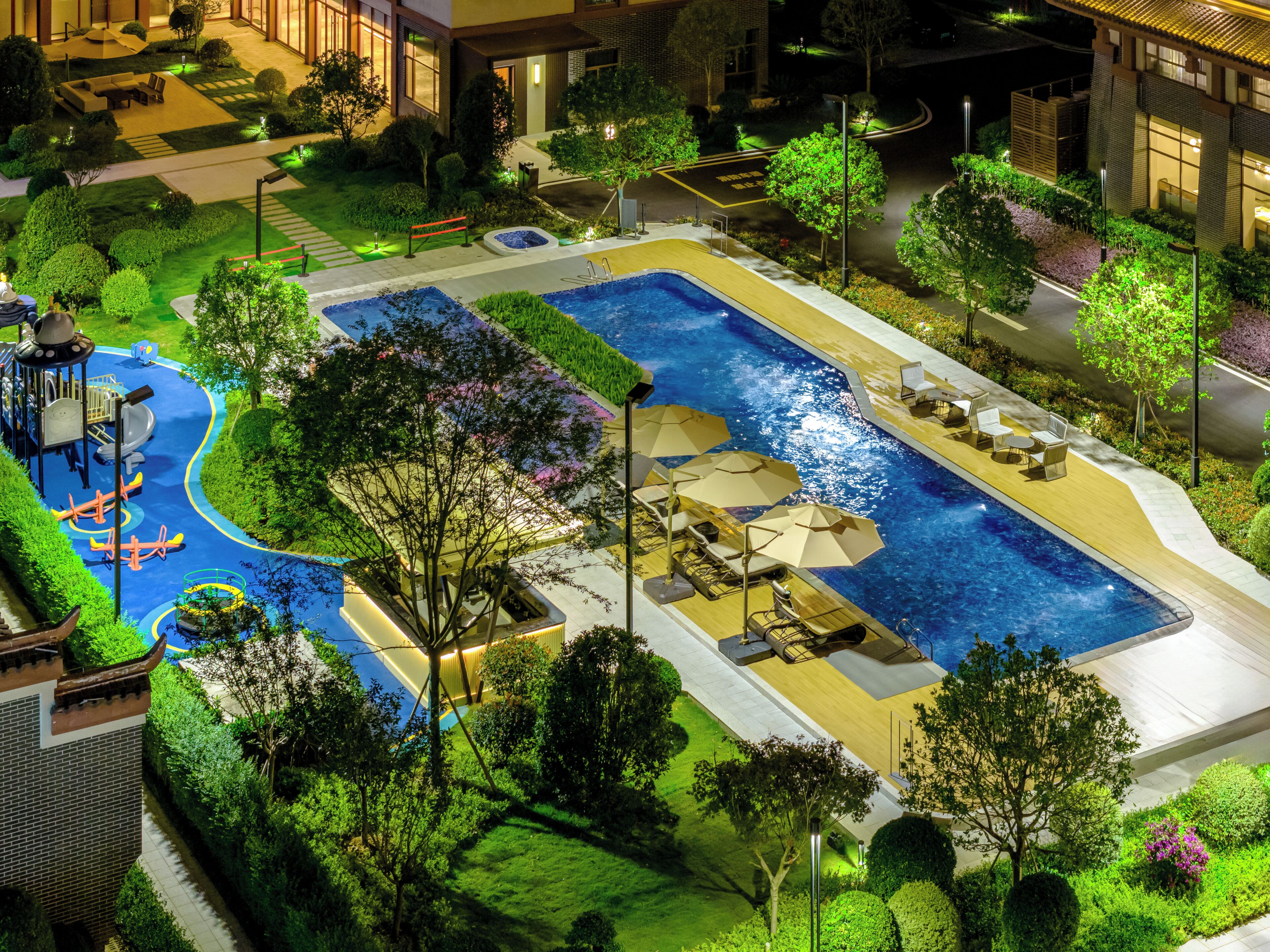 A large outdoor swimming pool with a children's play area, surrounded by well-maintained landscaping and modern buildings.