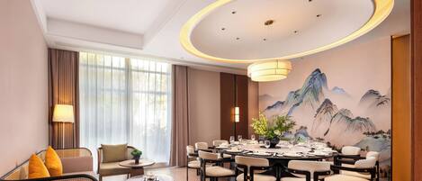 A hotel dining room with a round table set for six, surrounded by chairs, a sofa, and a lamp.