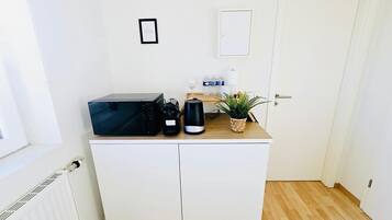 A small kitchenette with a microwave, coffee maker, and a potted plant on a white cabinet.