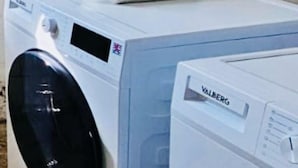 Two front-loading washing machines, one with a black door and the other with a white door, placed side by side on a concrete floor. - Chic Studio in Luxembourg city (Luxembourg City)