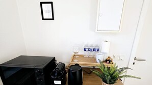 A kitchenette with a microwave, coffee maker, and kettle on a white countertop. There are water bottles, a glass, and a small plant on the counter. - Chic Studio in Luxembourg city (Luxembourg City)