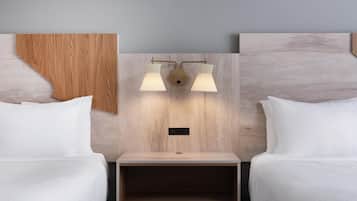 A hotel room with two beds, a wooden headboard, a nightstand, and a wall-mounted light fixture.