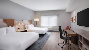 A hotel room with two beds, a desk, a chair, a TV, and a window with blinds.