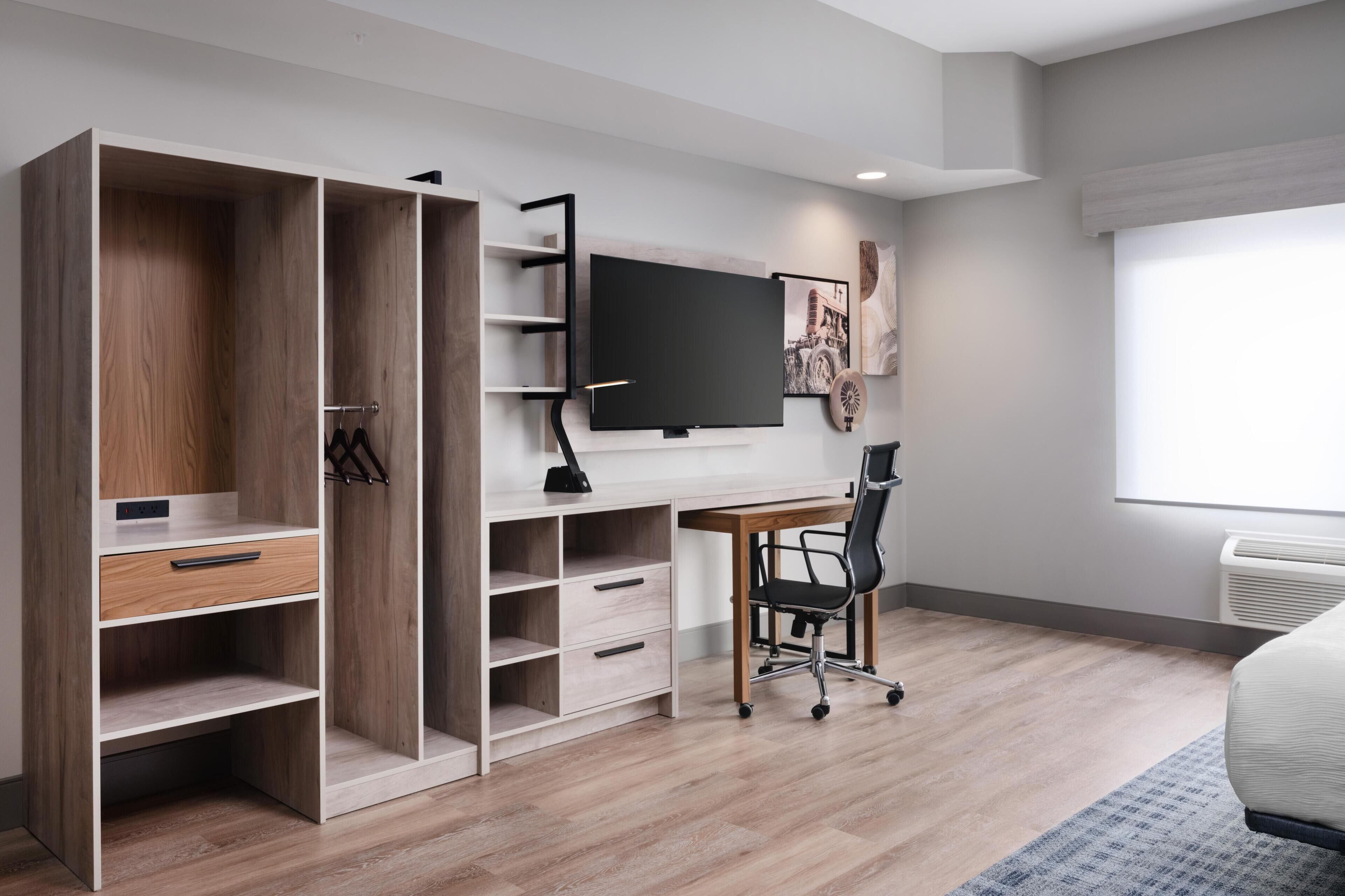 A modern bedroom with a bed, a desk with a chair, a wardrobe, and a TV.