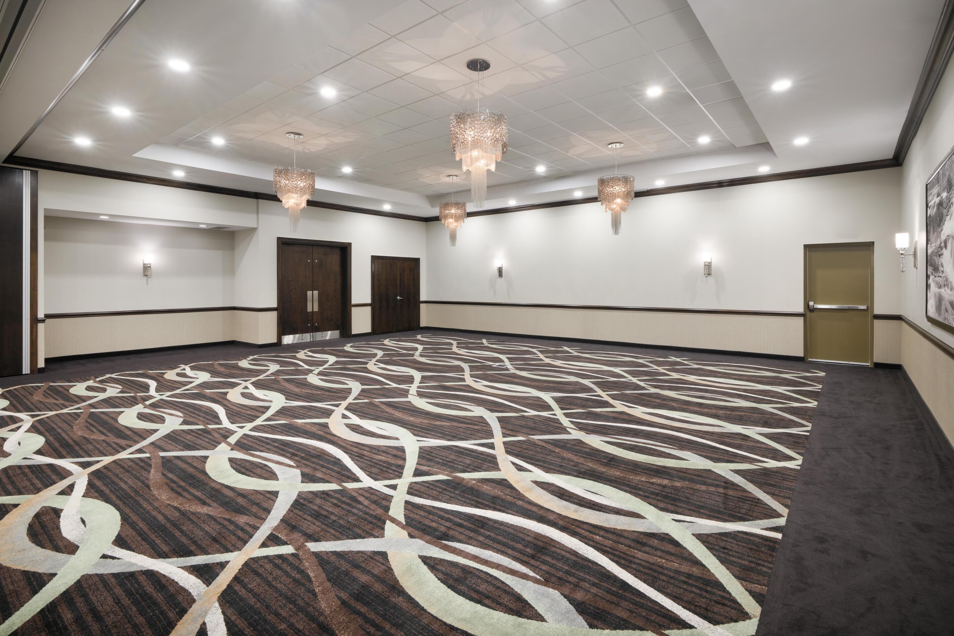 A large conference room with a patterned carpet, recessed ceiling lights, and a chandelier.
