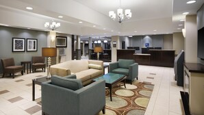 Un vestíbulo de hotel con un sofá, sillas, una mesa de centro, una recepción y un televisor.