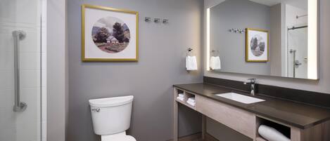 A modern bathroom with a toilet, sink, and mirror. There are framed pictures on the wall and a shower area.