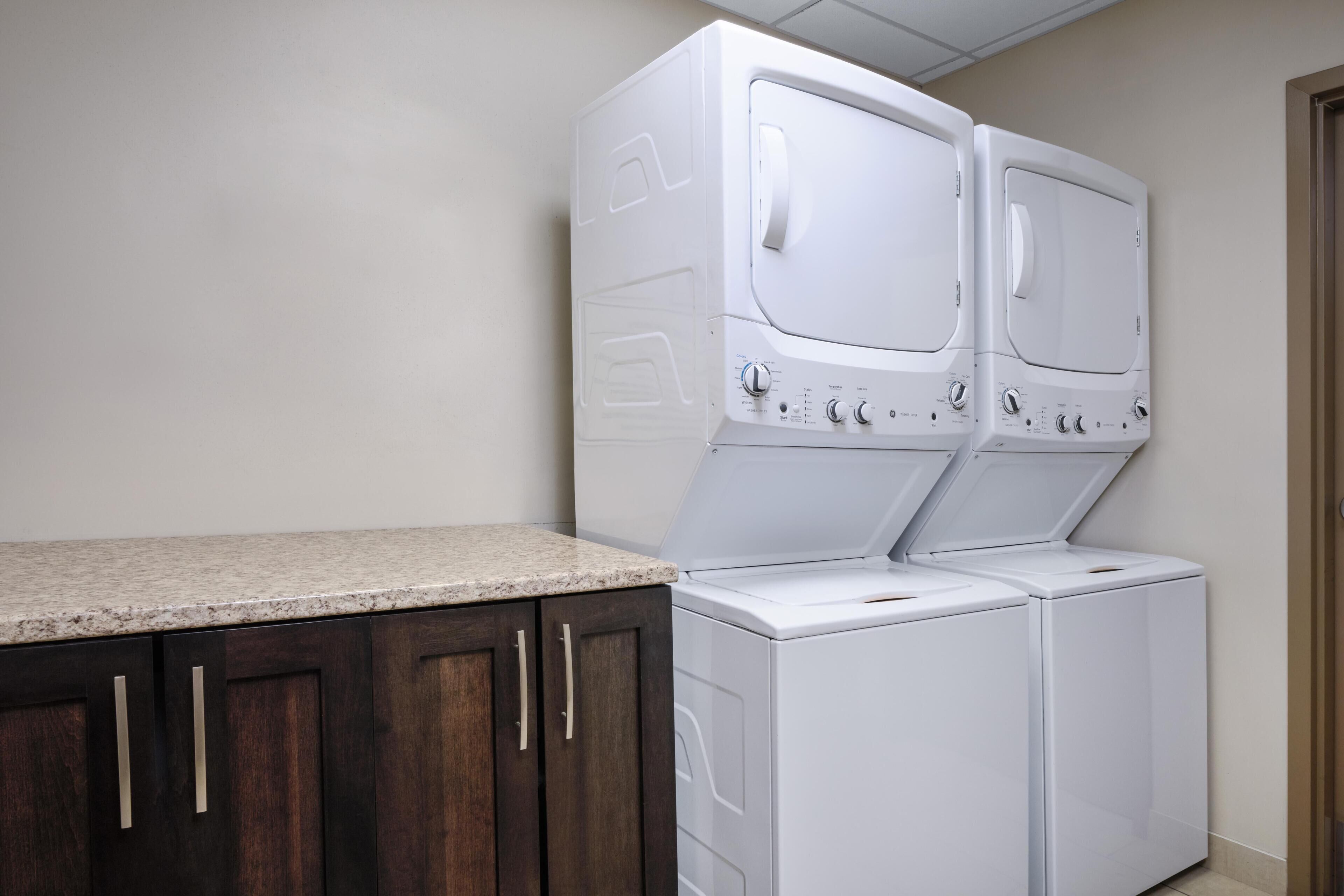 A laundry area with two stacked washers and dryers, wooden cabinets, and a granite countertop.