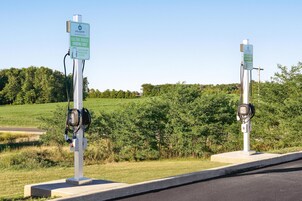 Two electric vehicle charging stations with signs indicating they are for electric vehicles only, set against a backdrop of a grassy field and trees.