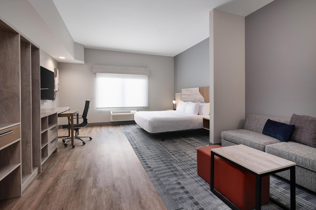 A modern hotel room with a bed, a sofa, a desk, and a wardrobe.