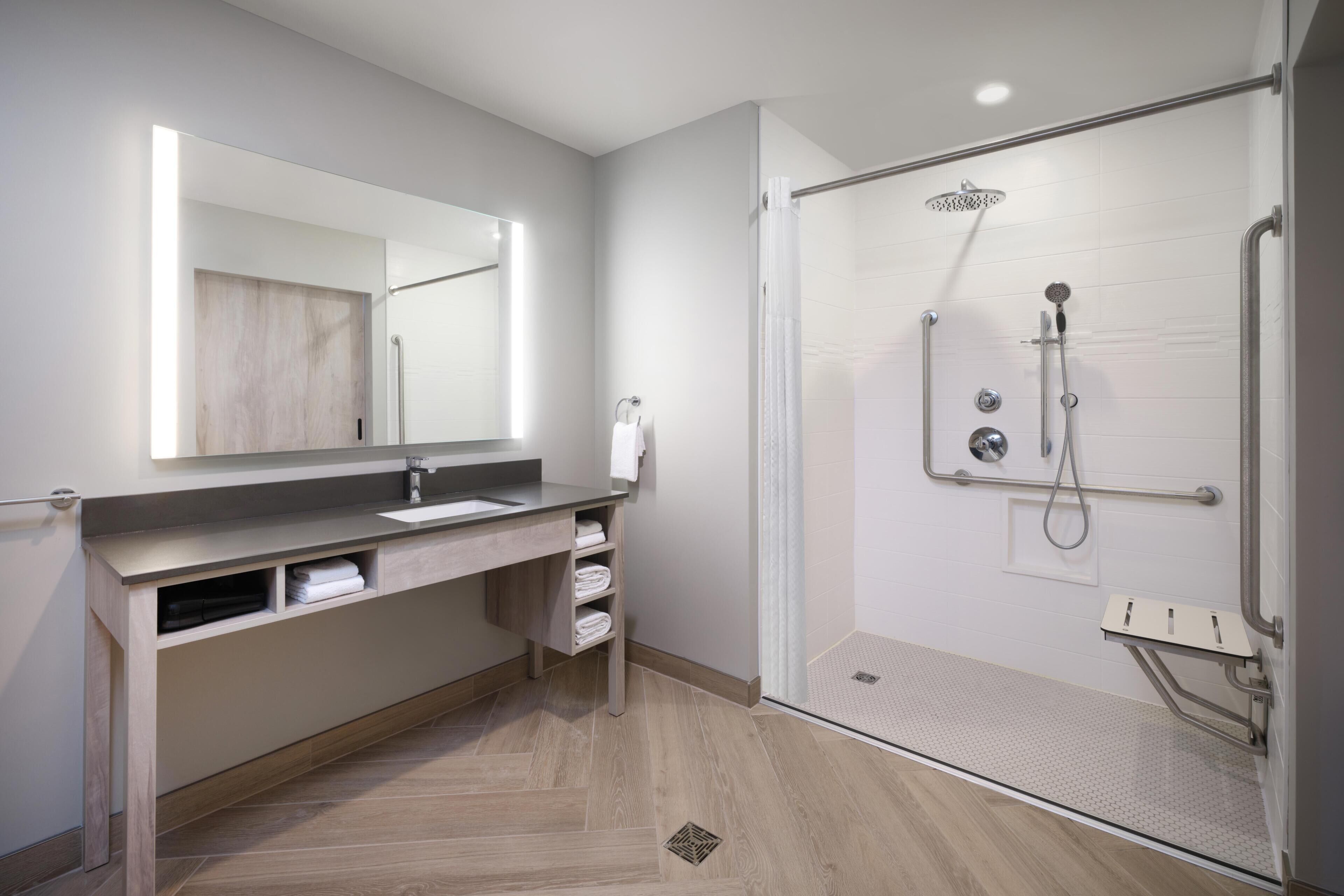 A modern bathroom with a large mirror, a shower with a handheld showerhead, and a sink with a towel rack.