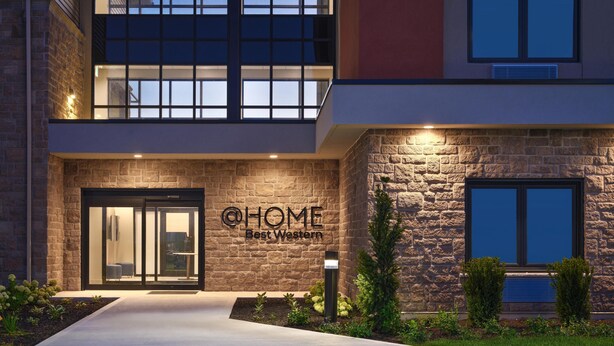 Un edificio moderno con fachada de piedra, entrada de vidrio y un letrero que dice 'HOME Best Western'.