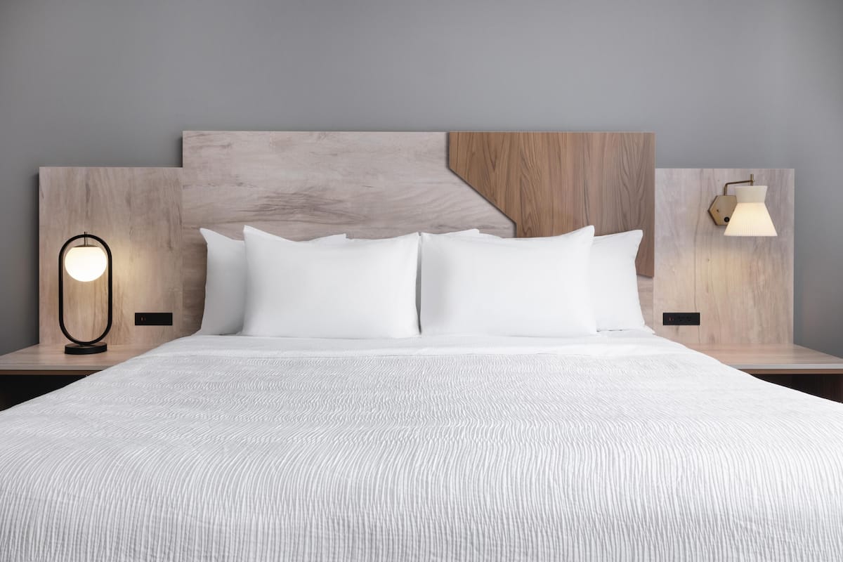 A neatly made bed with white linens, a wooden headboard, and two bedside lamps.