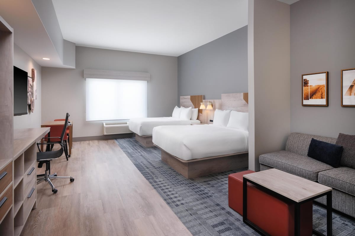 A hotel room with a bed, a sofa, a desk with a chair, and a TV.