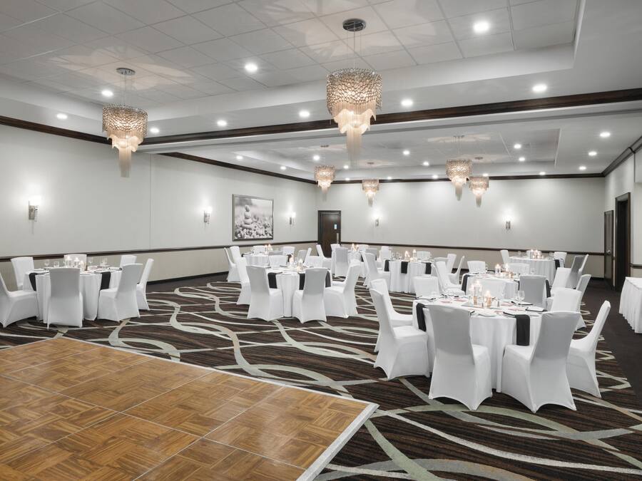 Un amplio salón de conferencias con mesas redondas, sillas blancas y candelabros.