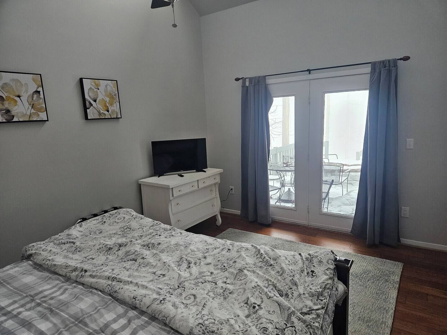 A bedroom with a bed, a dresser, a television, and a window with curtains.