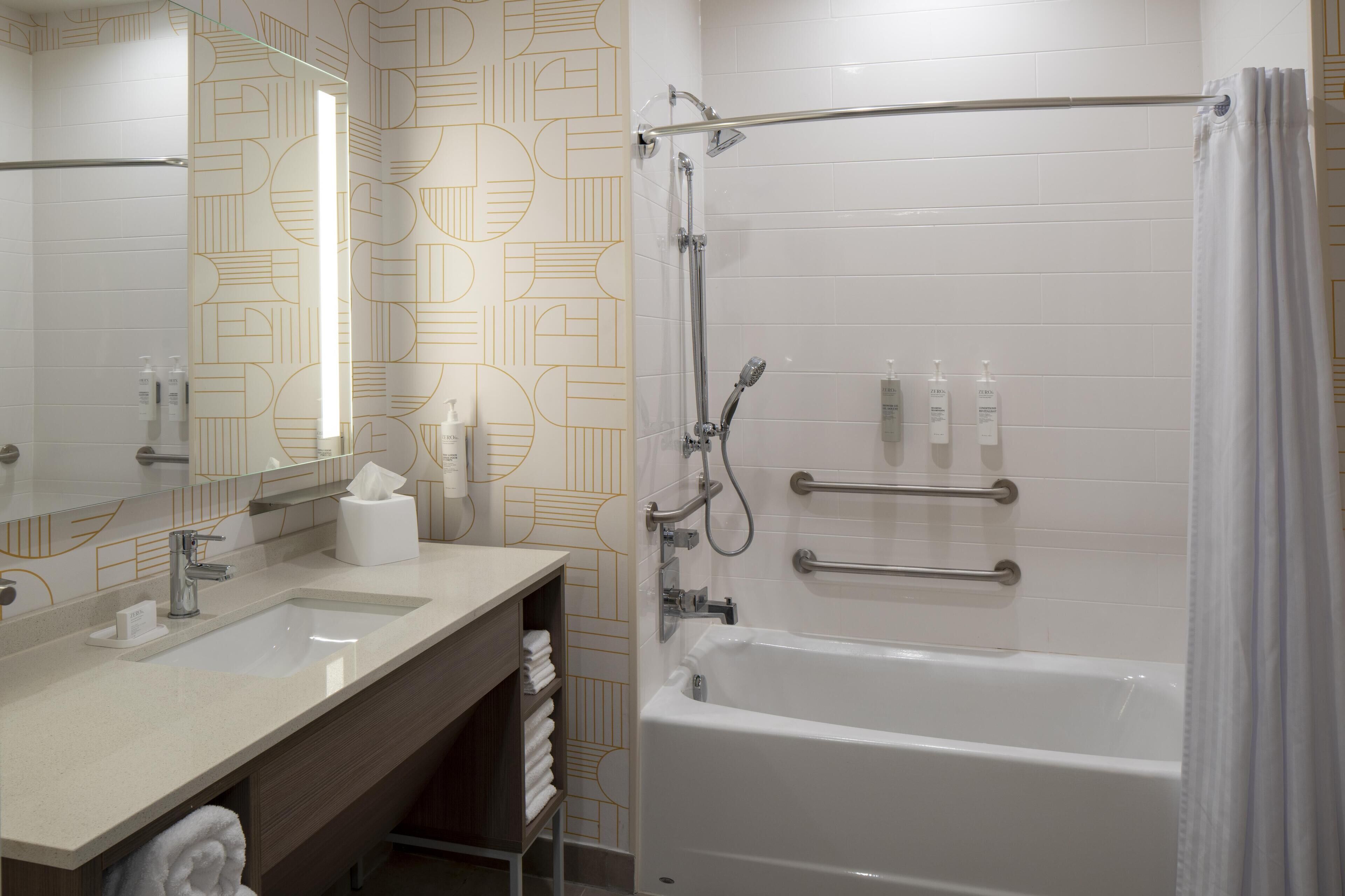A modern bathroom with a large mirror, a sink, a bathtub, and a shower.