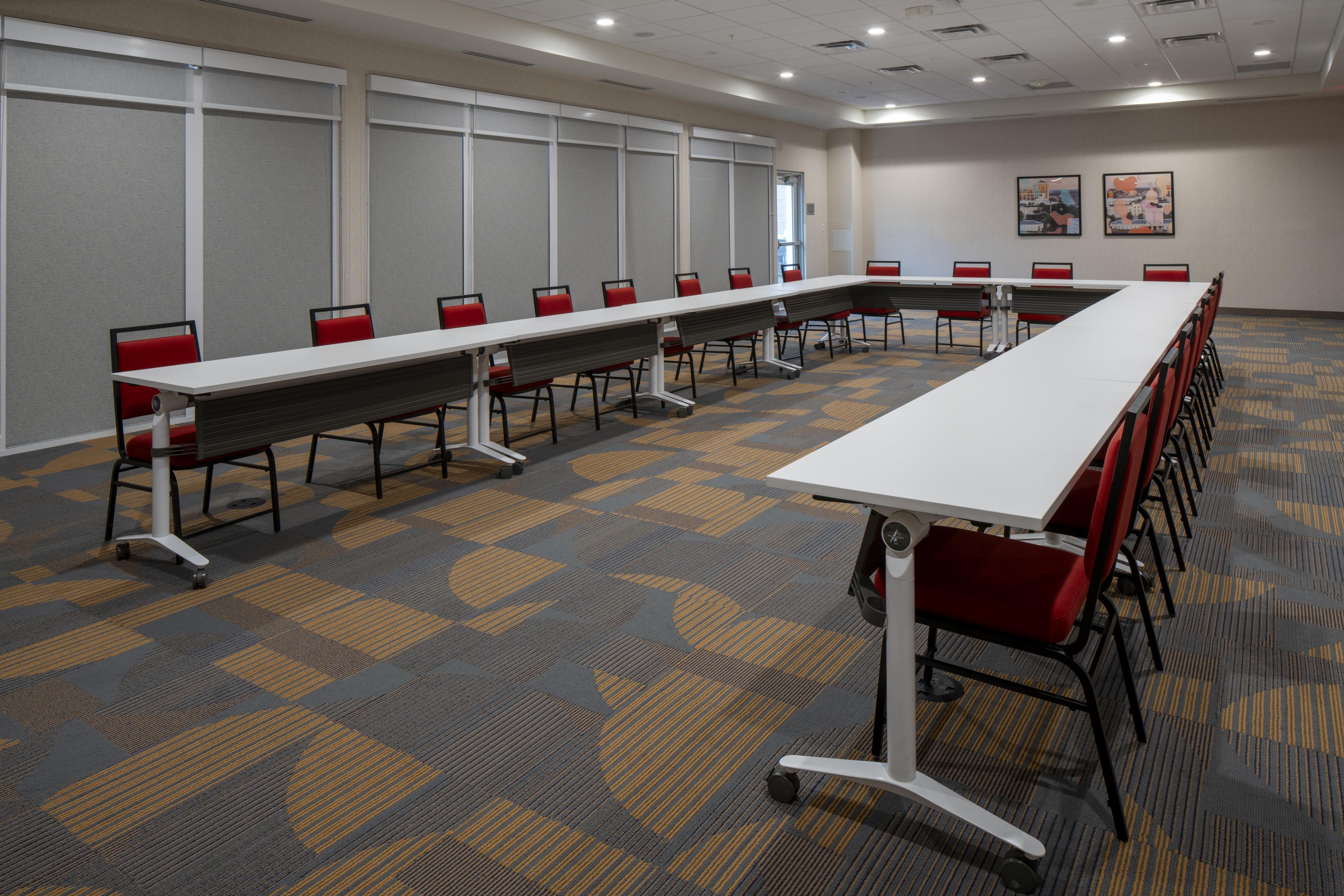 A conference room with a long table, red chairs, and a patterned carpet.