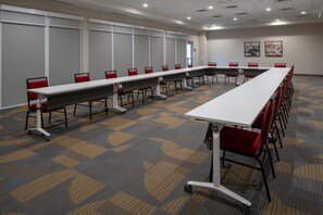 A conference room with a long table, red chairs, and a patterned carpet.