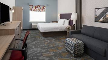 Une chambre d’hôtel avec un lit, un bureau, une chaise, un canapé et une moquette à motifs.