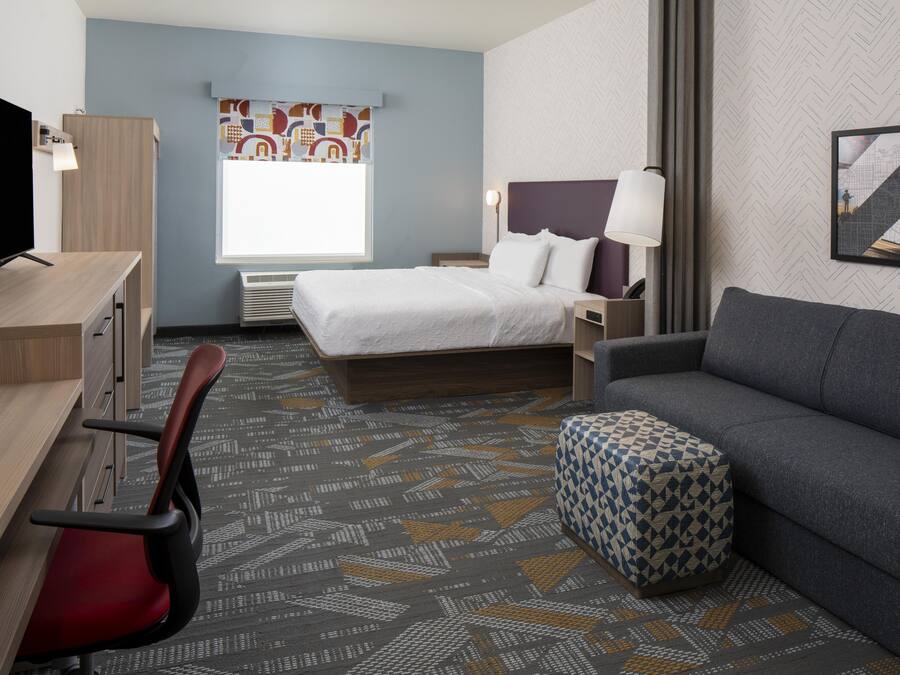 Une chambre d’hôtel avec un lit, un bureau, une chaise, un canapé et une moquette à motifs.