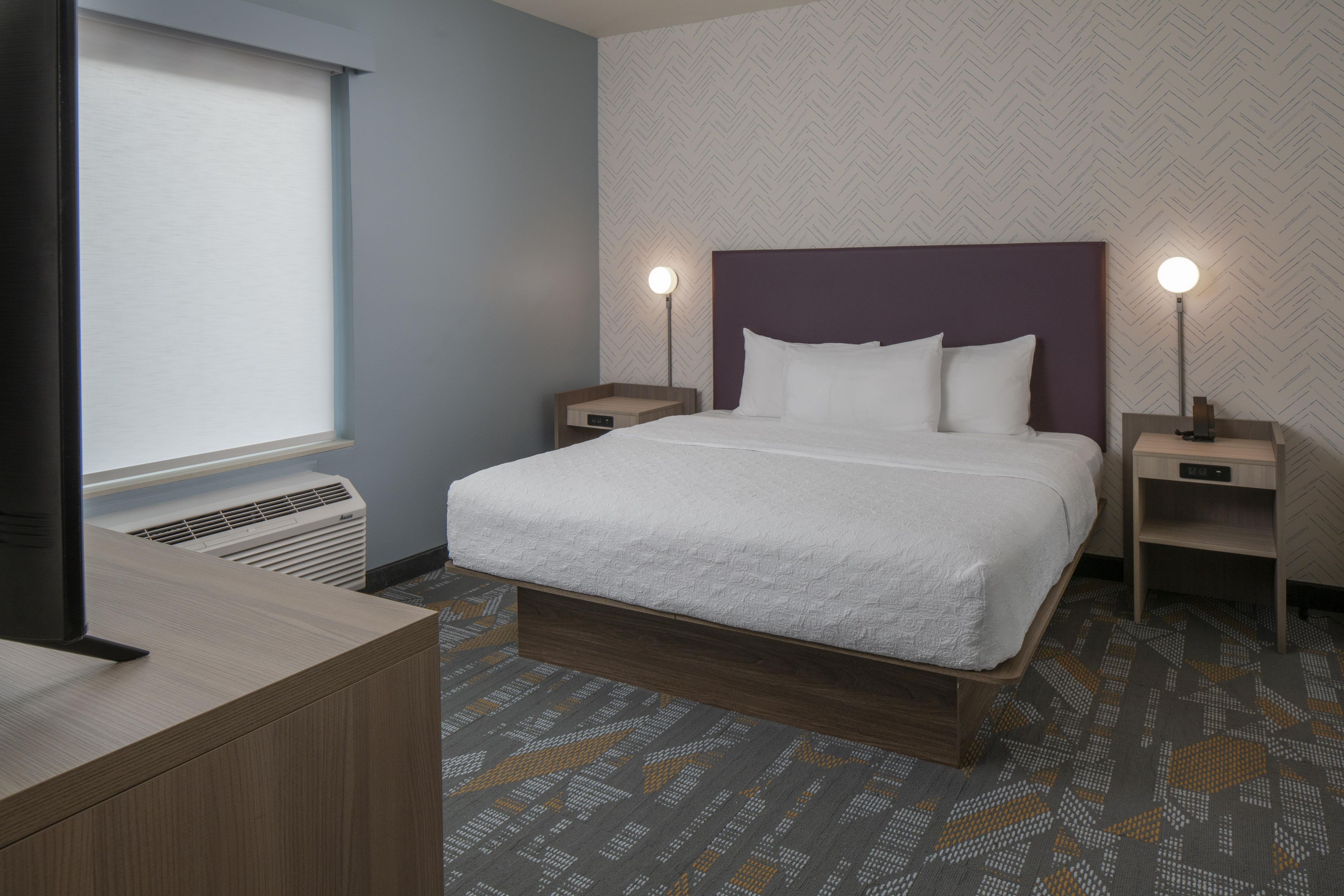 A hotel room with a bed, nightstands, a desk, and a window.