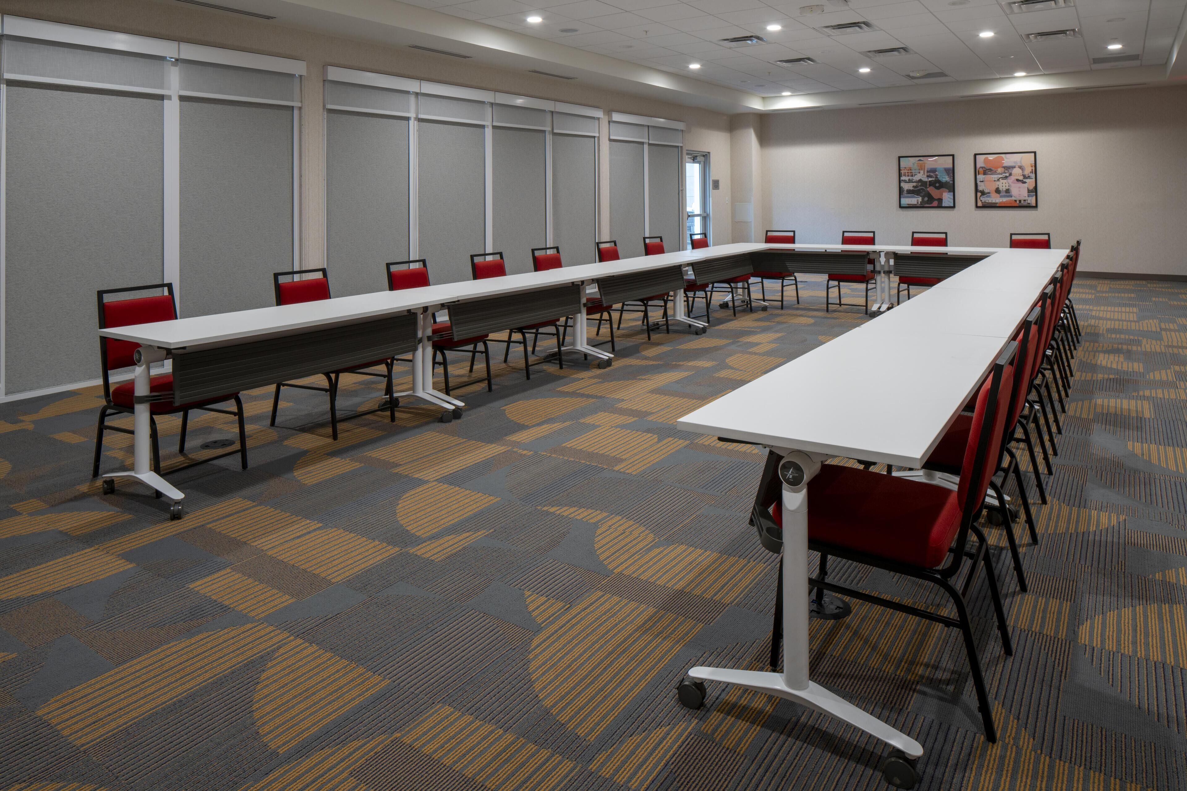 Une salle de conférence avec une longue table, des chaises rouges et un sol recouvert de moquette.