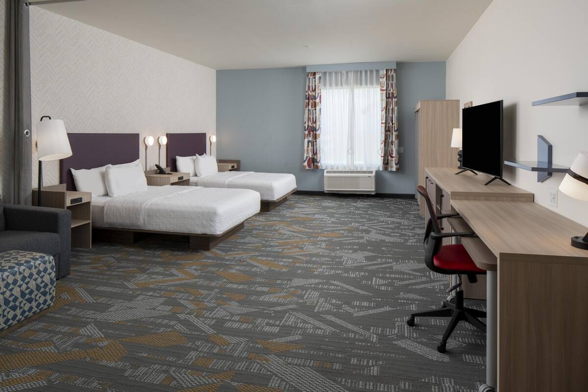 Quarto de hotel com duas camas, uma mesa, uma televisão e uma janela com cortinas.
