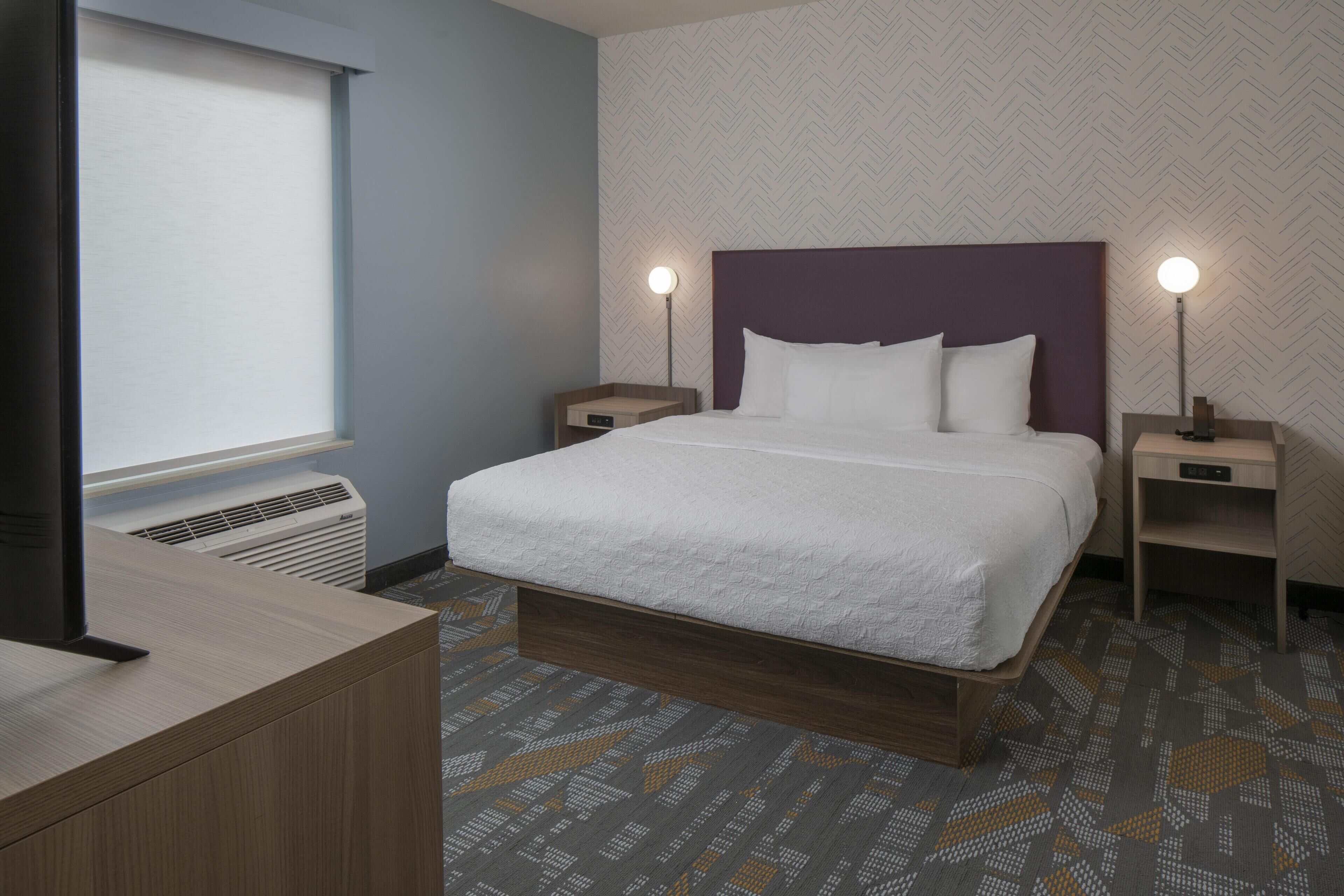 Una habitación de hotel con cama, mesitas de noche, escritorio y ventana.