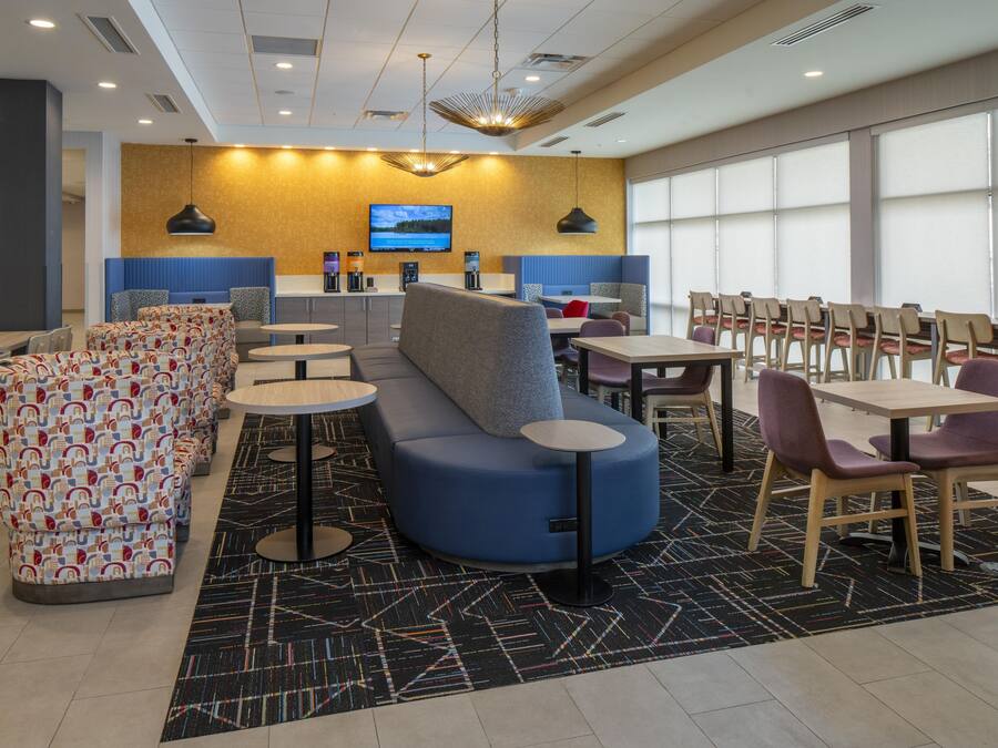A modern hotel lobby with seating areas, a TV screen, and a coffee bar.