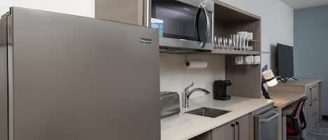 A kitchenette with a refrigerator, microwave, toaster, sink, and cabinets.