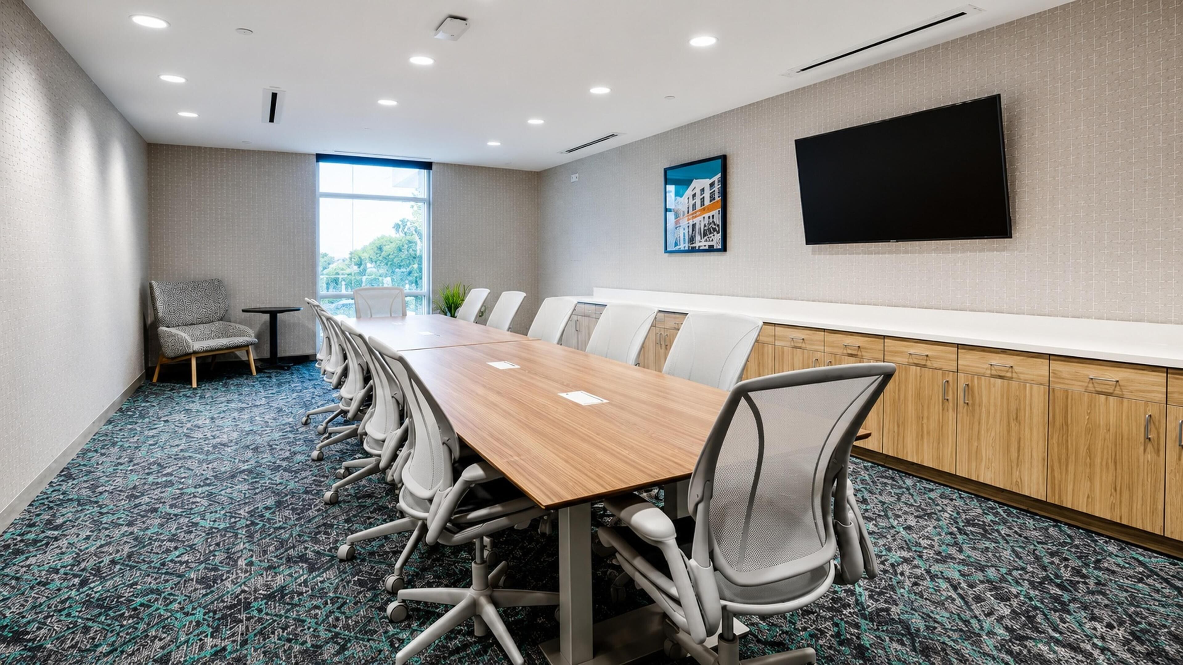 A conference room with a long table, chairs, a TV, and a window.