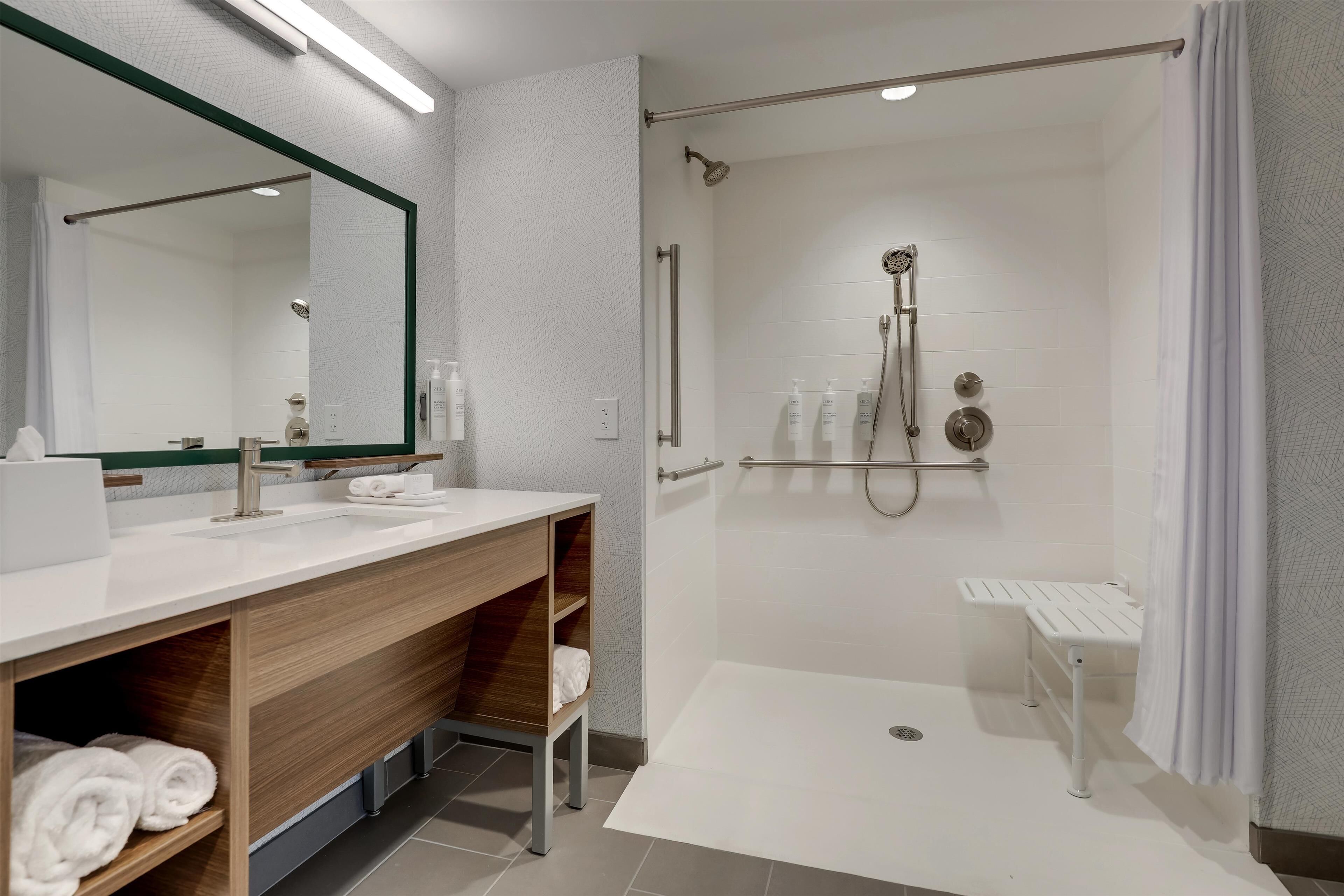 A modern bathroom with a walk-in shower, a large mirror, and a vanity with a sink and towel rack.