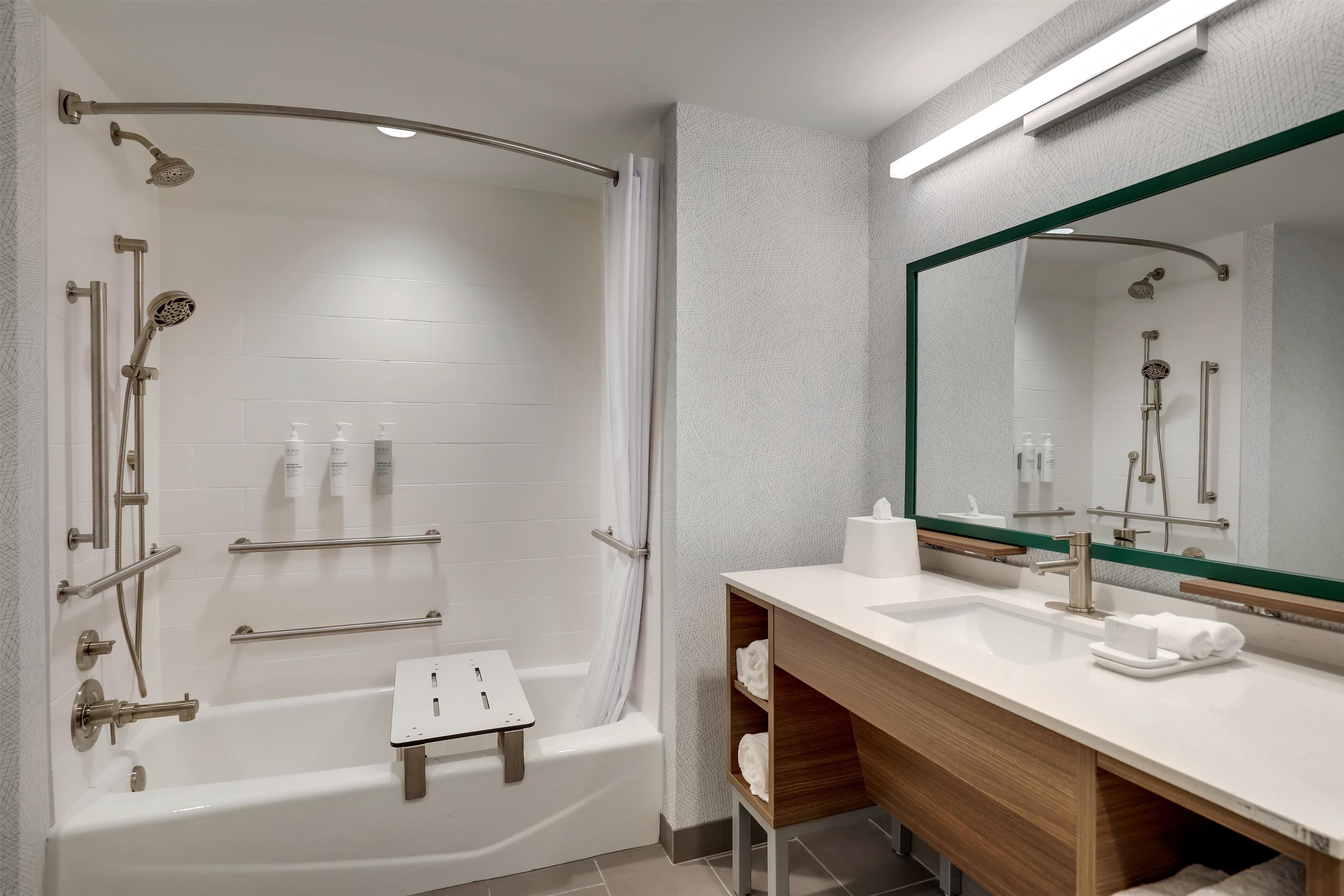 A modern bathroom with a walk-in shower, a vanity with a mirror, and a small stool.