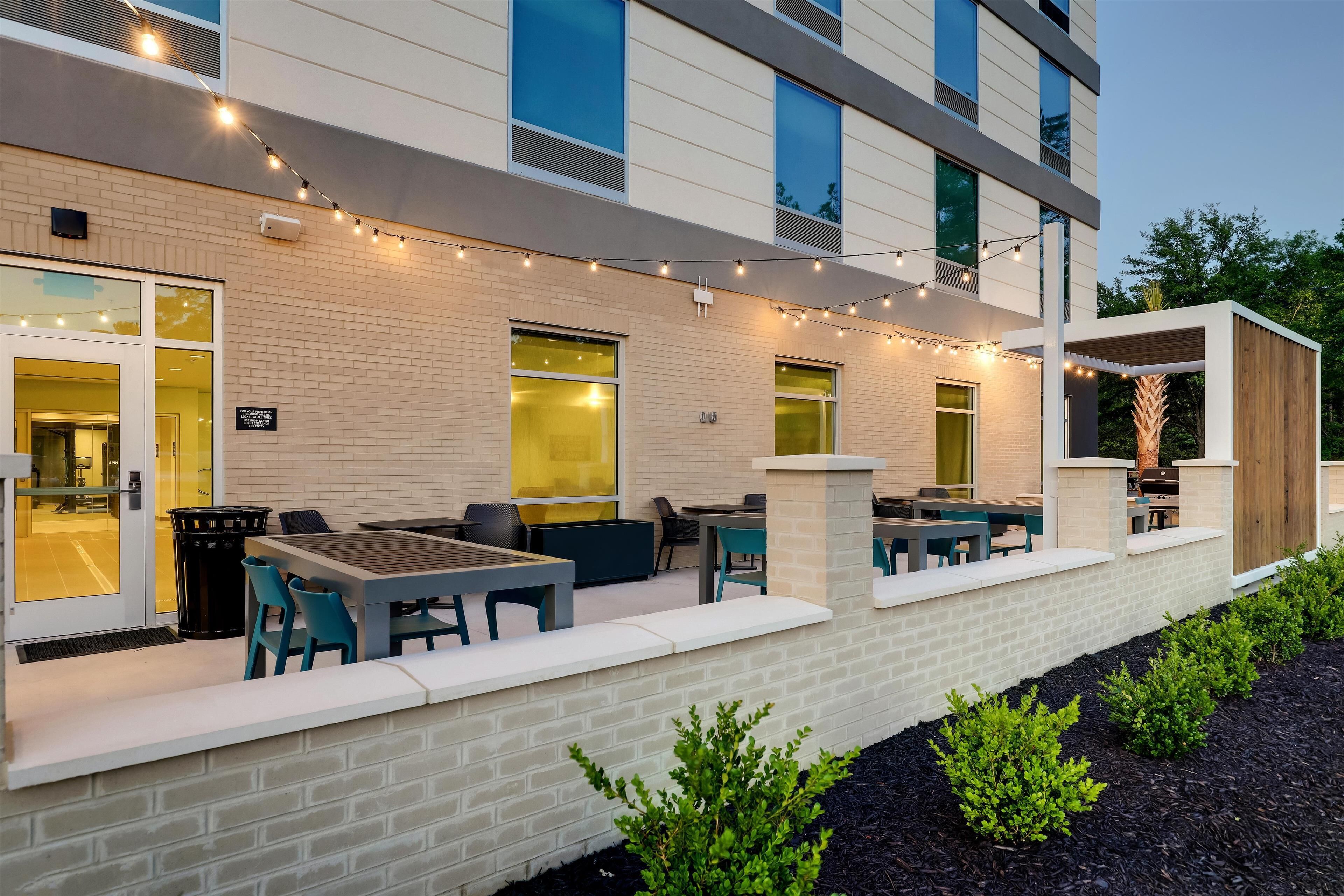 An outdoor patio area with seating and string lights, a brick wall, and a small garden.