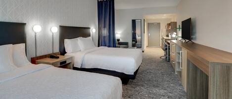 A hotel room with two beds, a desk, a TV, and a bathroom visible in the background.