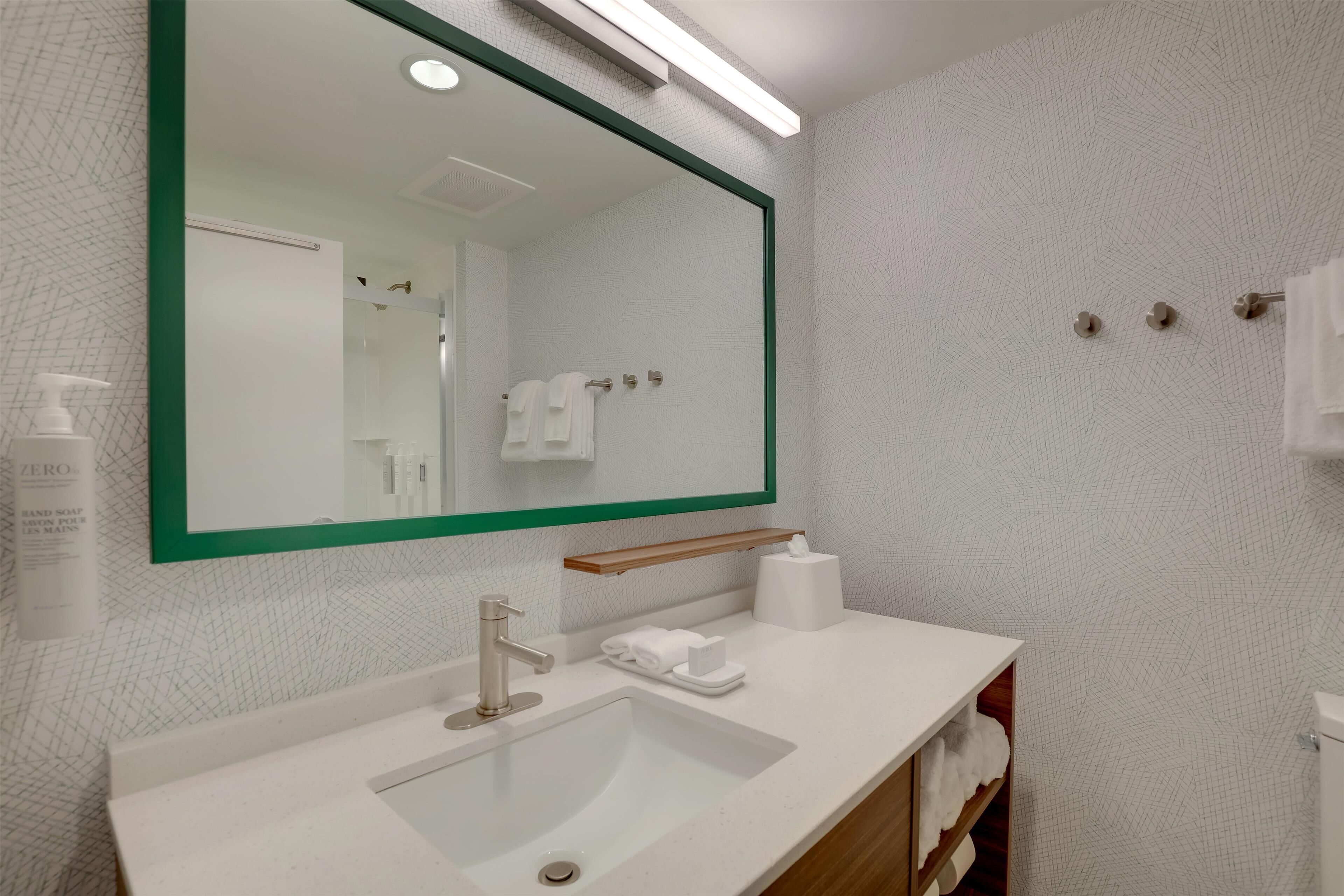 A bathroom with a large mirror, a sink, a towel rack, and a soap dispenser.